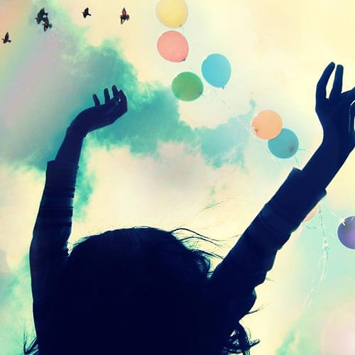Silhouette of a woman with their hands up and colorful balloons flying in the sky above.