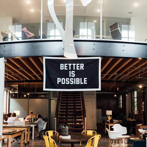 A modern office with many open chairs and tables with a banner across the entrance saying better is possible.