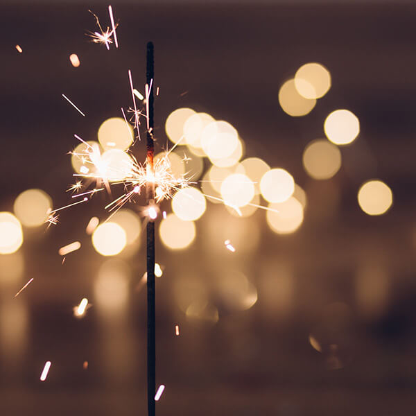 The tip of an ignited sparkler shining brightly against a night sky.
