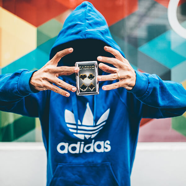 A magician wearing a large Adidas brand hoodie floating a stack of cards with his hands.